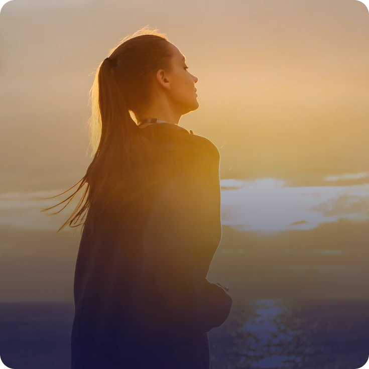 Woman in profile gazing at sunset over a calm landscape